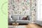 Graues Sofa vor einer Wand mit Blumenprinttapete, dazu ein runder Couchtisch aus Holz, Tischdeko sowie ein grauer Teppich; daneben schöne Blumenvasen in Grüntönen.