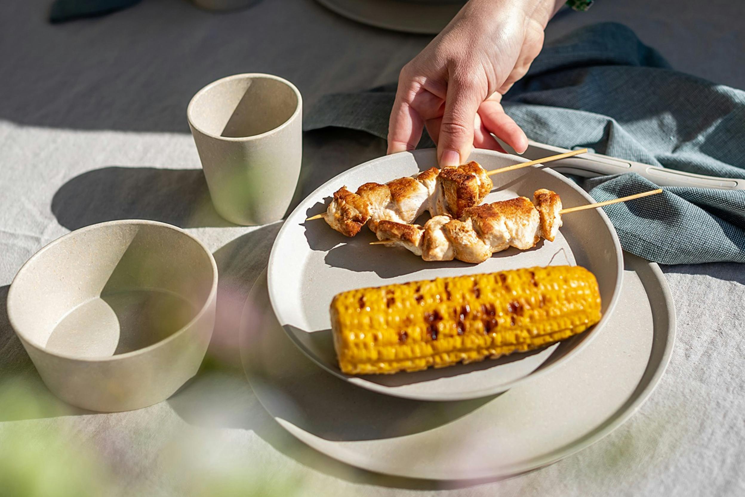 Gegrillte Hähnchenspieße mit Maiskolben, serviert auf beigem Picknickgeschirr