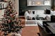 Modernes Wohnzimmer mit klassischer Weihnachtsdeko in Rot, Grün und Gold am geschmückten Tannenbaum. Dahinter ein modernes, graues Loungesofa vor dunkler Akzentwand.