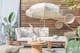 Outdoor-Loungemöbel der Serie LEXI by BUTLERS aus hellem Akazienholz mit weißen Polstern, dazu ein passender Tisch dekoriert mit weißen Vasen, ein weißer Sonnenschirm mit Fransen, ein Outdoor-Teppich und Pouf aus Jute sowie Wanddeko, Pflanzenkorb und Windlicht in Flechtoptik.