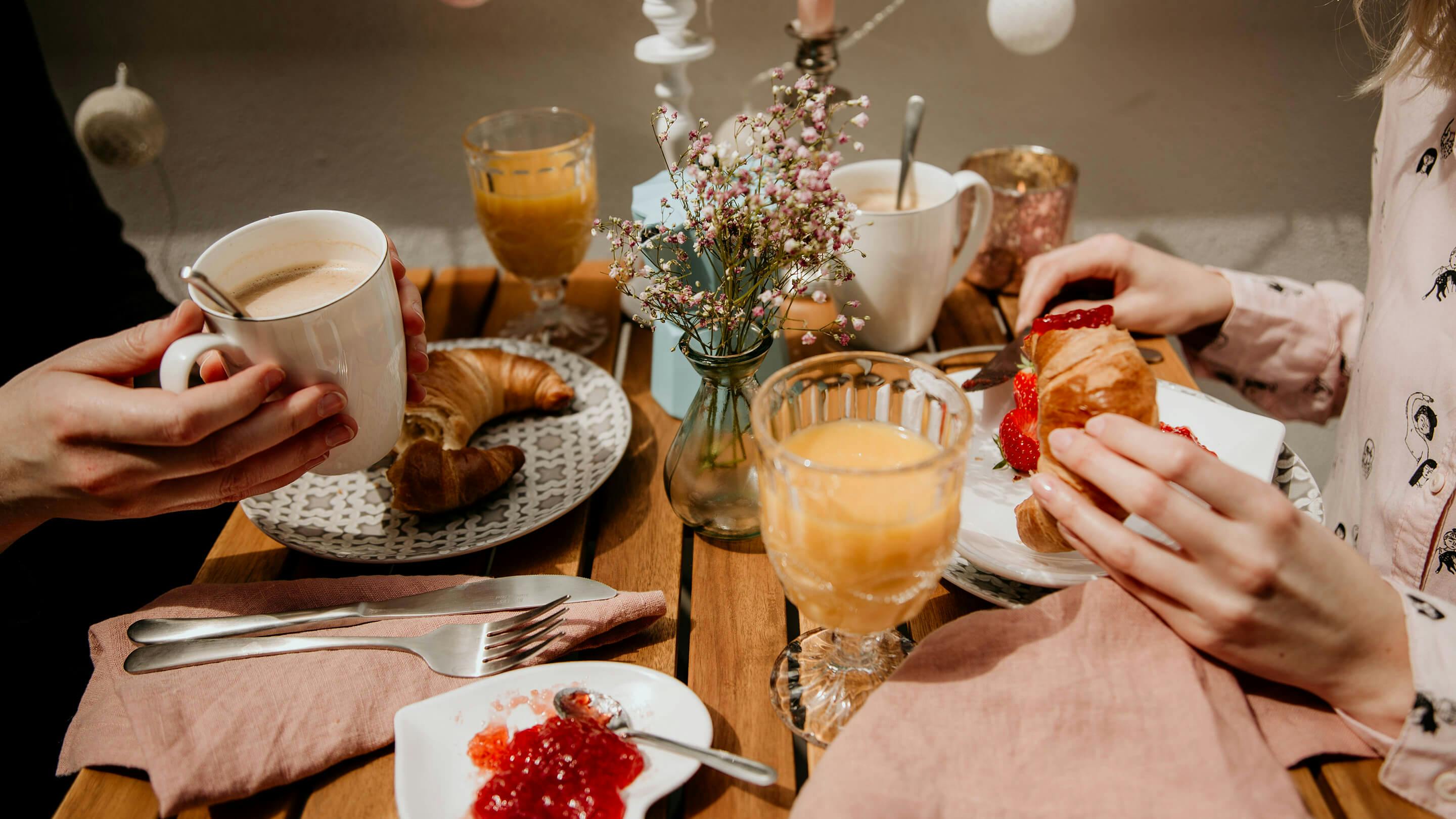 Gedeckter Balkontisch mit Frühstück: Croissants, Marmelade, Gläser mit Saft, Becher mit Kaffee etc. (Marke: Butlers).