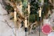 Des bougies blanches dans des chandeliers dorés et noirs devant une couronne de Noël sur un mur en marbre ; à côté, des bougies colorées en spirale ainsi que des bougies lisses.