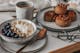 Frühstücksset in Grau (Butlers) auf Tablett: kleiner Teller, Schale mit Müsli, großer Teller mit Zimtschnecken, Kaffeebecher.