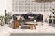Terrasse im orientalischen Stil mit einem Loungesofa mit grauen Polstern und gemusterten Kissen in Erdtönen, dazu ein kupferfarbener Tisch mit Terrazzo-Platte, ein Sonnenschirm, Kakteen und sonstige Grünpflanzen.