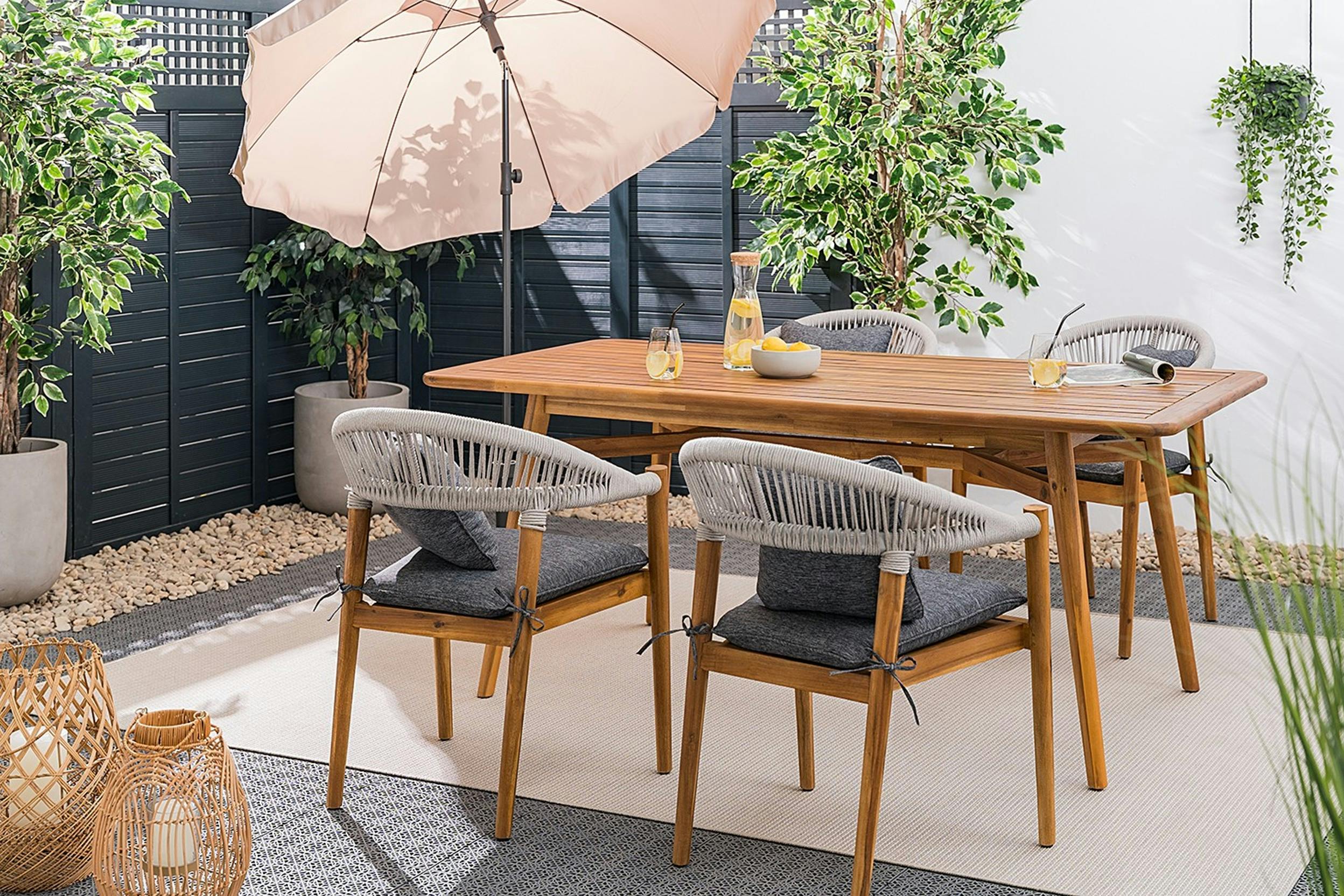 Essgruppe aus Holz mit 4 Stühlen auf einer Terrasse mit Outdoor-Teppich und hellem Sonnenschirm