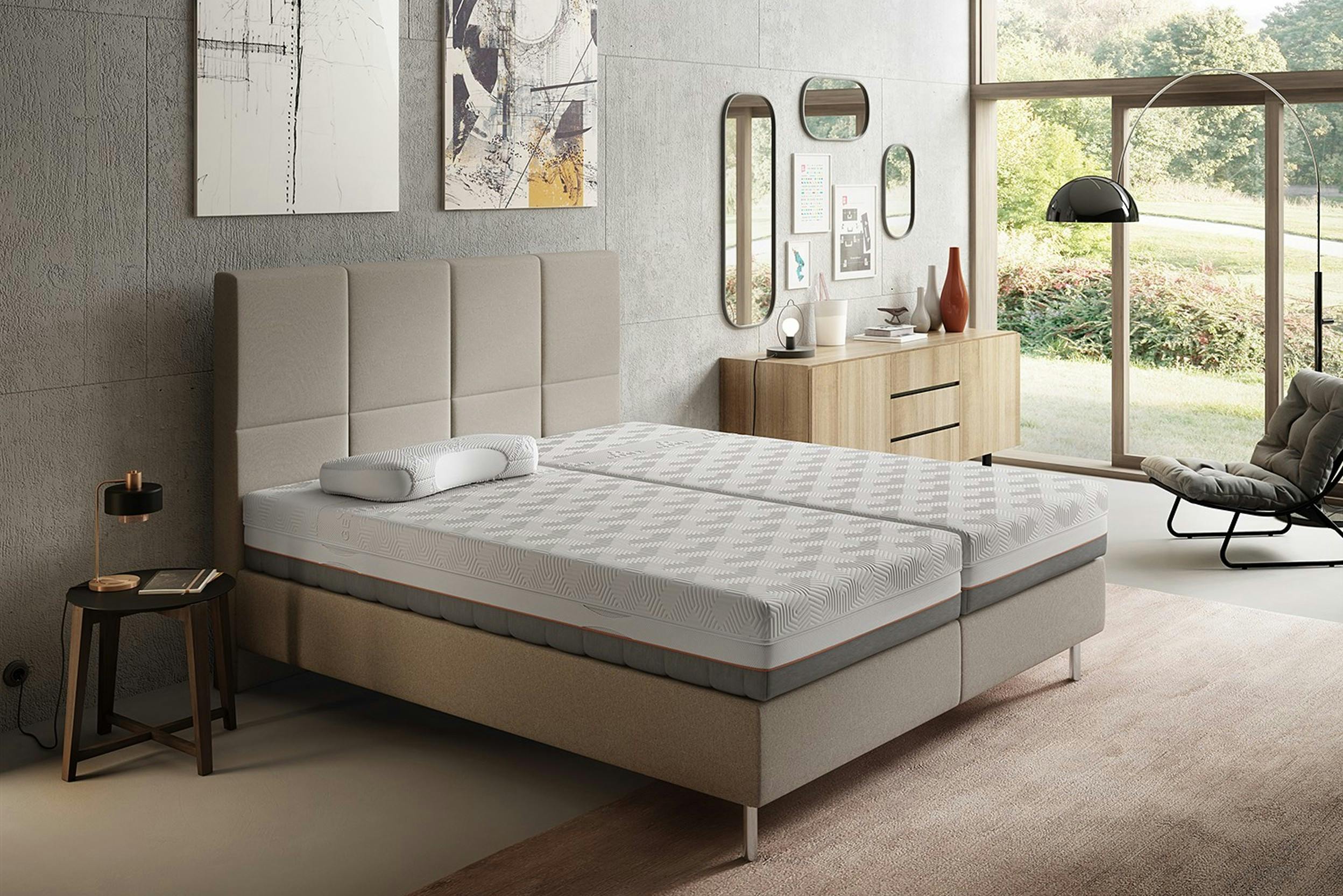 Slaapkamer in grijs- en beigetinten met gestoffeerd bed en gelmatrassen.