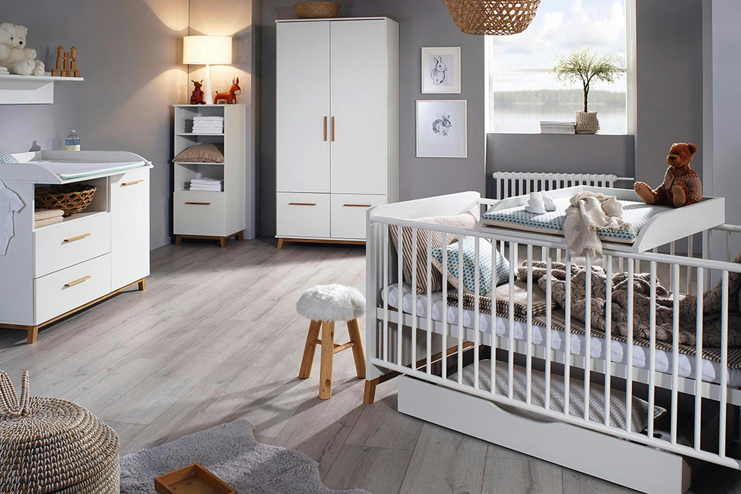 Kinderzimmer grau gestrichen und sanft beleuchtet mit Wickeltisch und Baby Gitterbett und Teddy