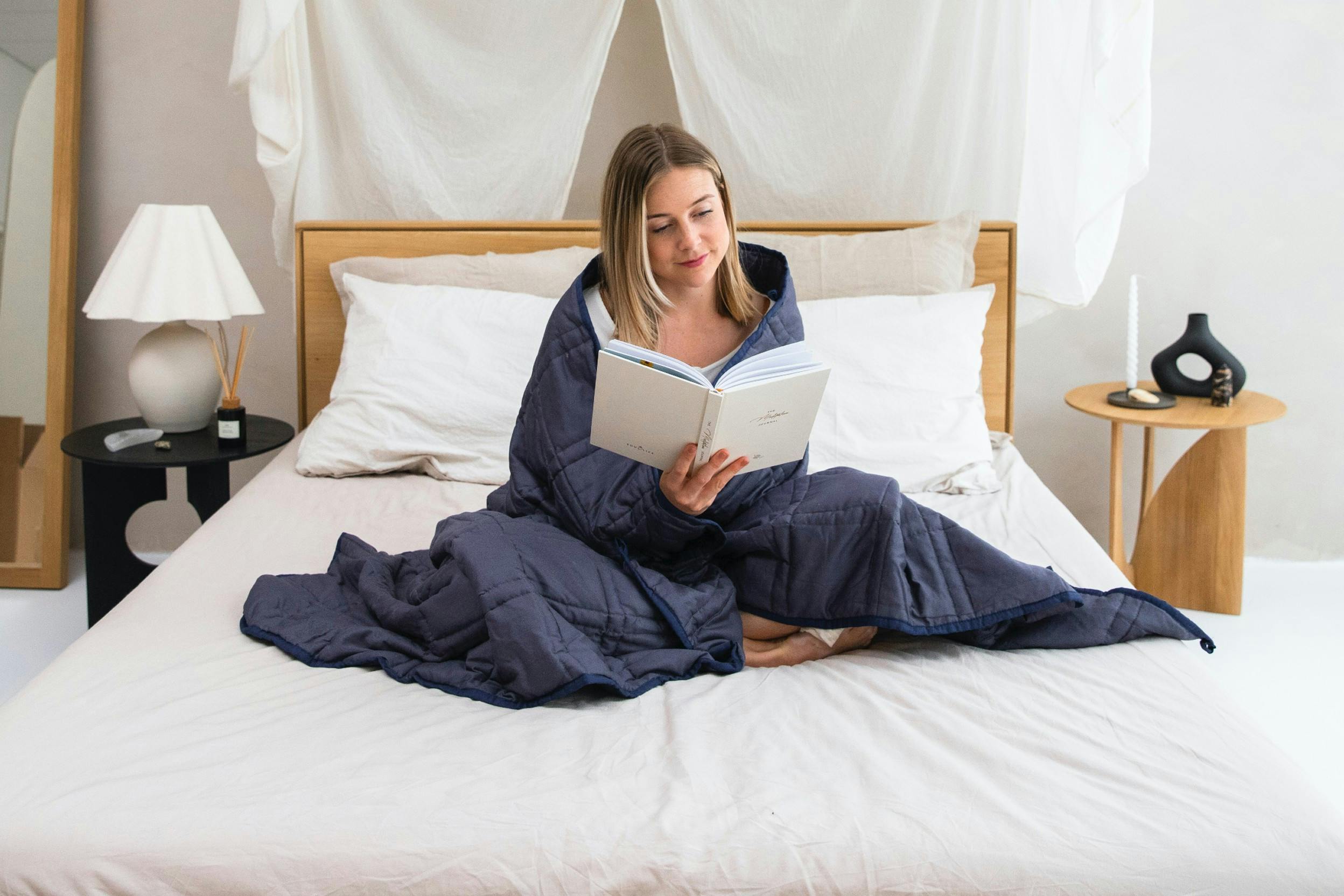 In een deken gewikkelde vrouw leest een boek op bed.
