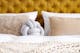 Slaapkamer in de Scandi stijl met mosterdgeel gestoffeerd bed van fluweel met chesterfieldknopen en veel zacht textiel