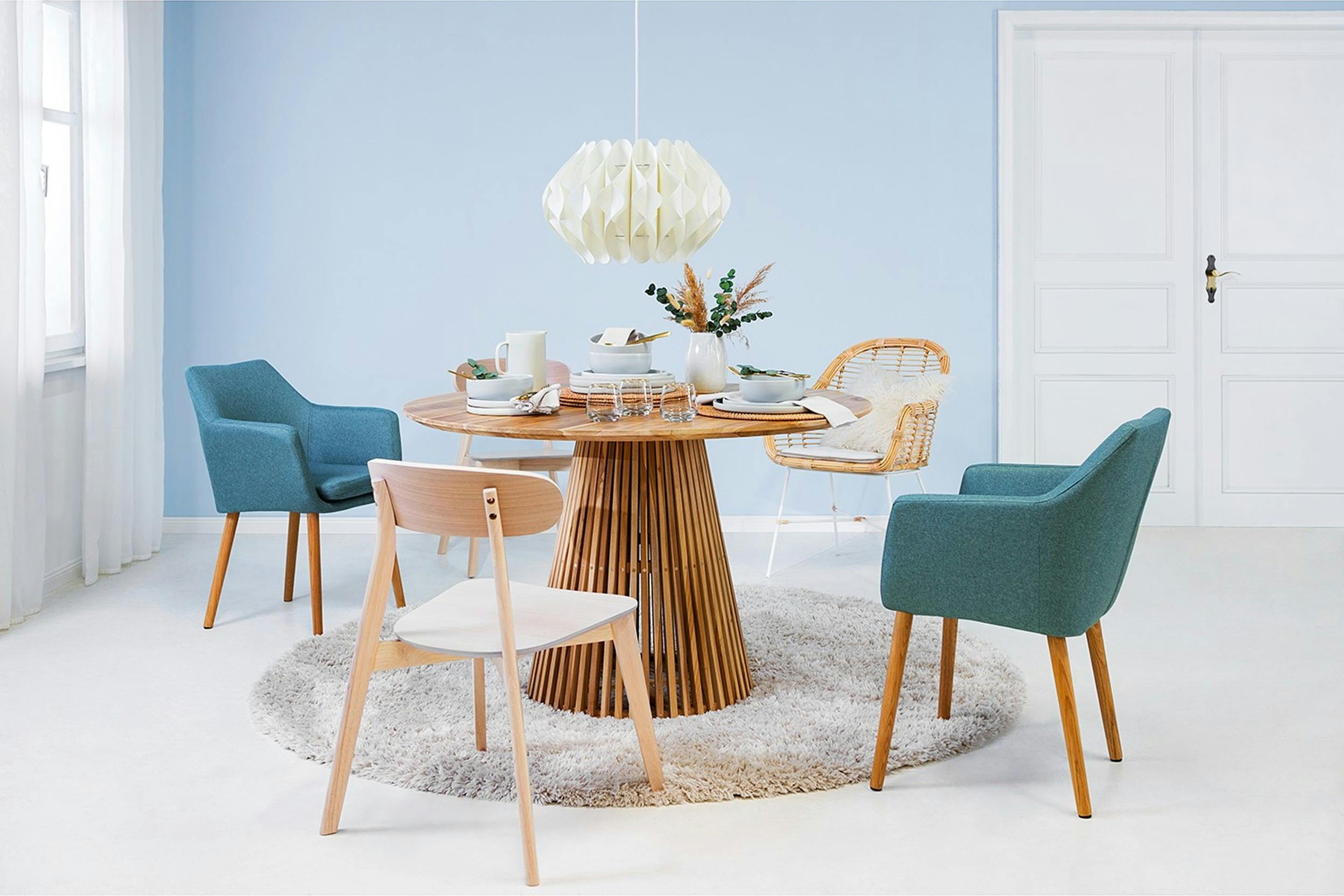Moderner runder Esstisch mit 5 verschiedenen Stühlen vor einer hellblauen Wand