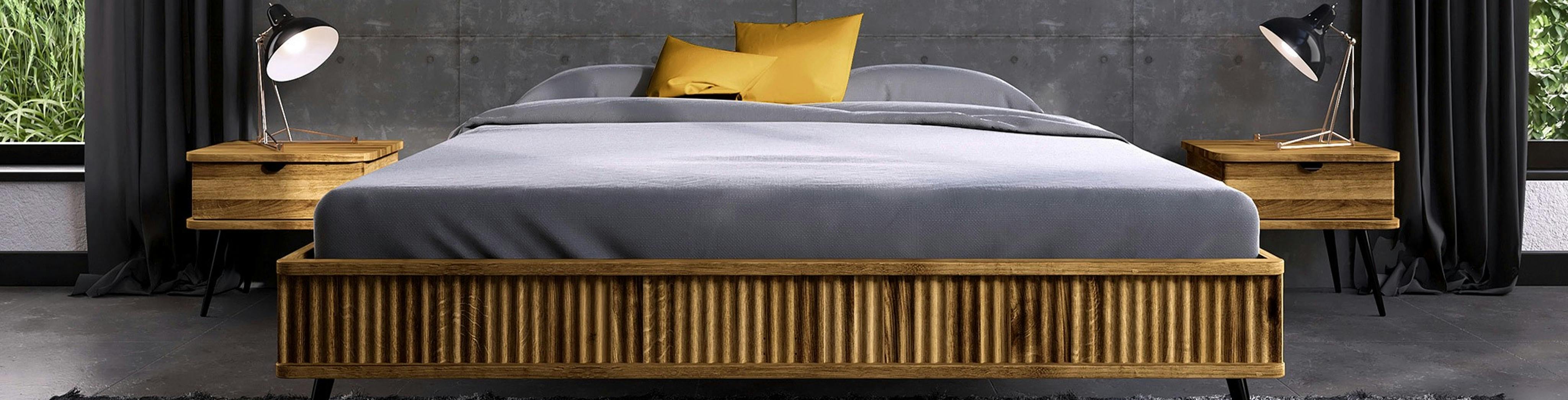 Lit futon en bois clair avec literie gris clair et jaune, avec 2 tables de chevet du même bois, dans une chambre au sol et murs sombres.