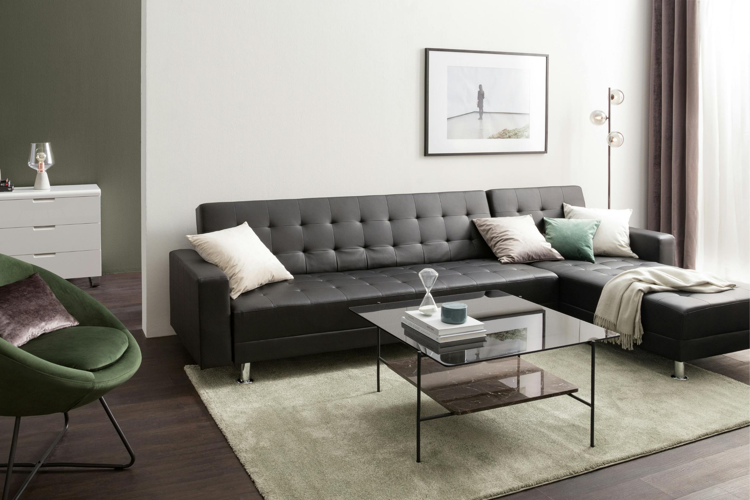 Schwarzes Ledersofa in Wohnzimmer mit Grüntönen kombiniert und Couchtisch mit glänzender Glasplatte