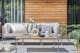 Modulare Loungemöbel der Serie TEAKLINE by BUTLERS für Terrasse, Garten und Balkon aus Teakholz mit einem Gestell aus Edelstahl, hellgrauen Polstern und kombiniert mit Outdoor-Teppich und Kissen in Anthrazit