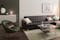 Canapé d'angle en cuir, table basse en verre, tapis, fauteuil en velours vert de style rétro et enfilade blanche moderne.