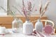 Heller Holztisch mit drei Trockenblumensträußen in großen Vasen arrangiert