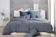 Geräumiges Bett mit grauer Baumwollbettwäsche vor einer grauen betonartigen Wand