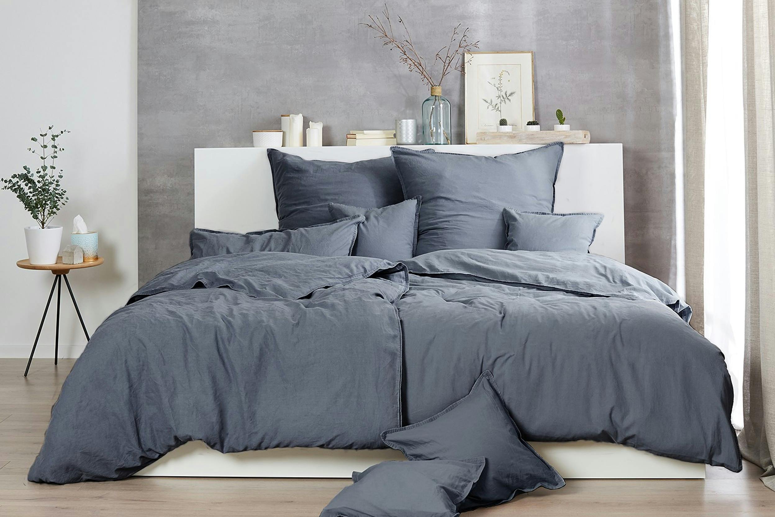 Geräumiges Bett mit grauer Baumwollbettwäsche vor einer grauen betonartigen Wand
