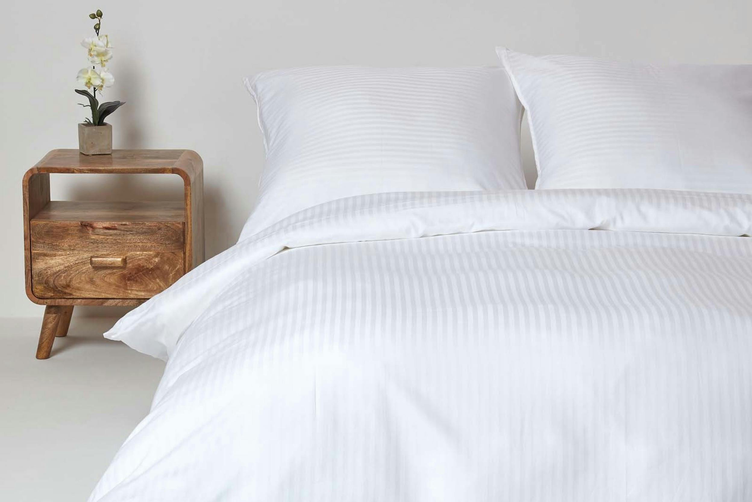 Damast-Bettwäsche im edlen Streifendesign neben einem modernen Holz-Nachttisch