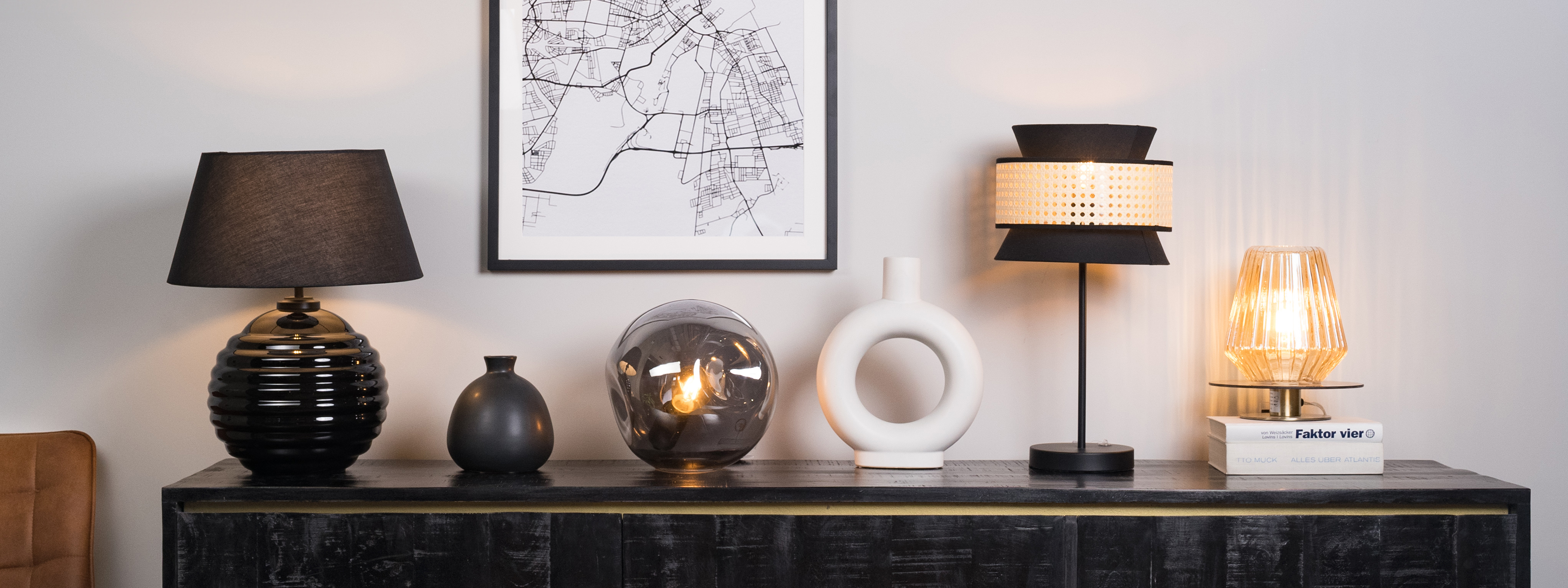Schwarzes Sideboard mit einer schwarzen, runden Tischleuchte, einer schwarzen Kugellampe aus Glas, einer schwarzen Tischlampe mit Rattan und einer geriffelten Tischleuchte aus Klarglas, dazu eine schwarze und eine weiße Vase.
