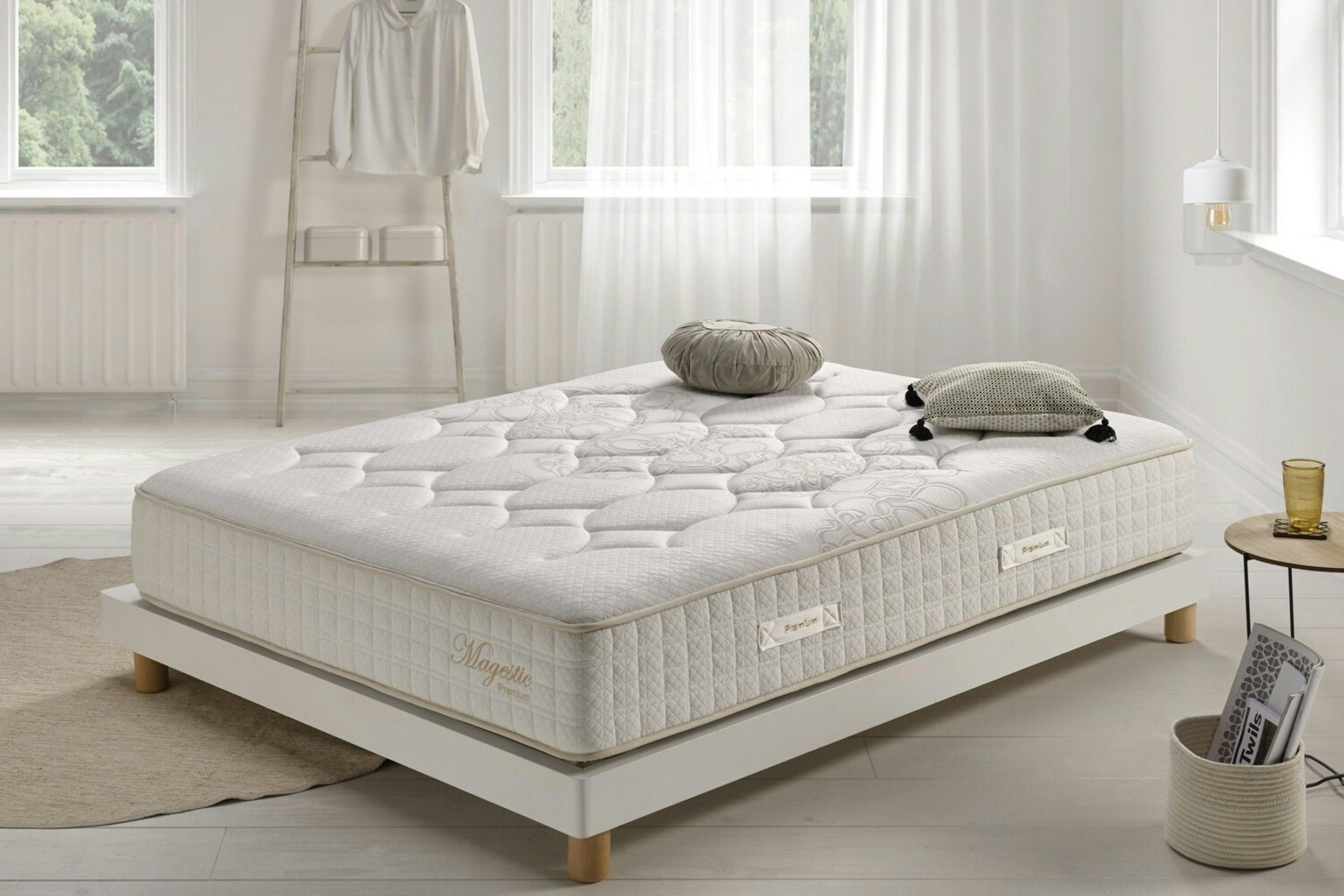 Lichte slaapkamer met onopgemaakt bed, erg dik matras en decoratieve kussens.