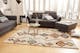Salon avec meubles gris, parquet de bois clair, petite table basse ronde en verre, et tapis beige à motifs colorés