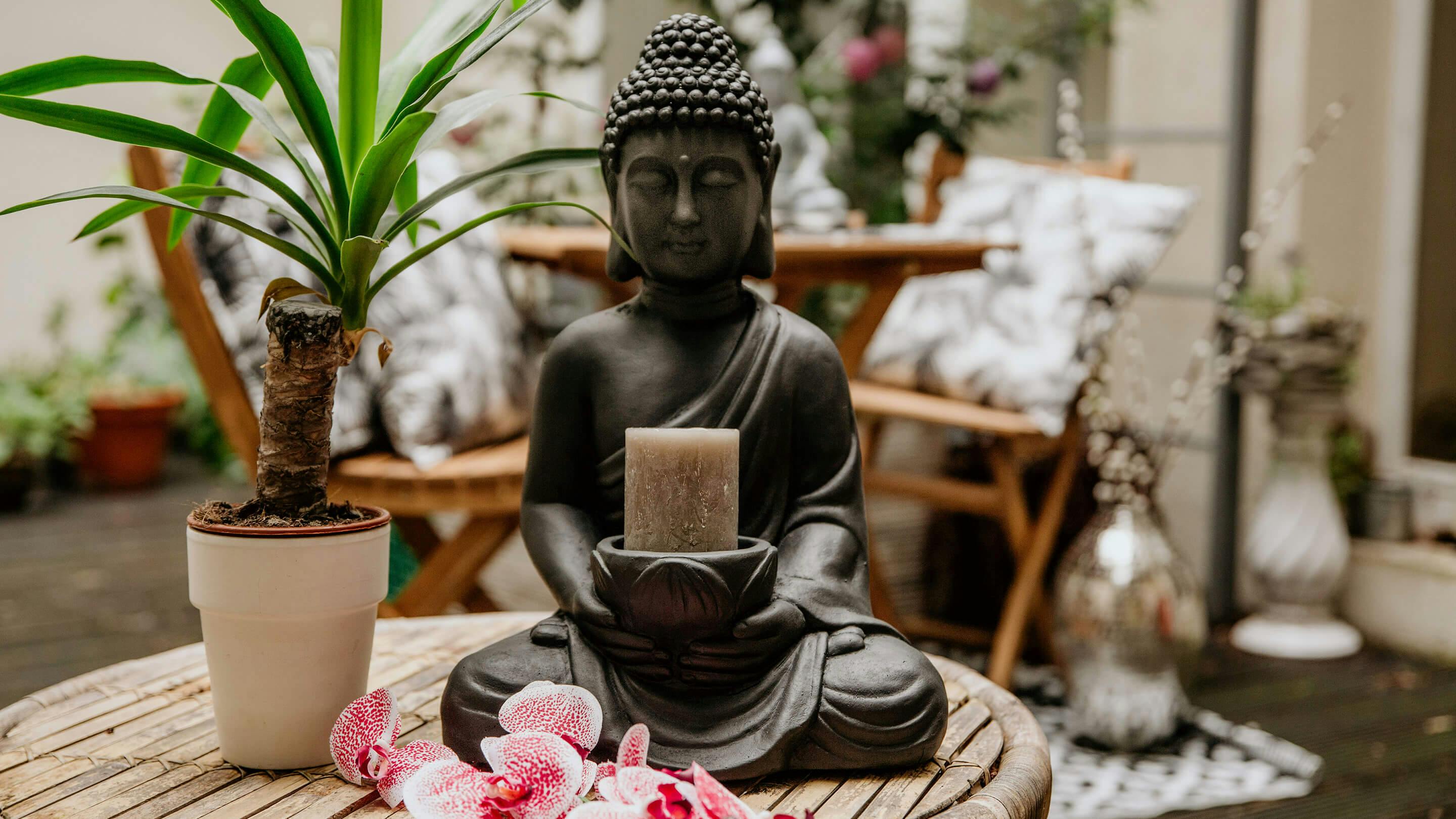 Buddha-Figur als Kerzenhalter, grüne Pflanzen in kleiner Vase in Beige auf einem Outdoor-Beistelltisch (Marke: Butlers).