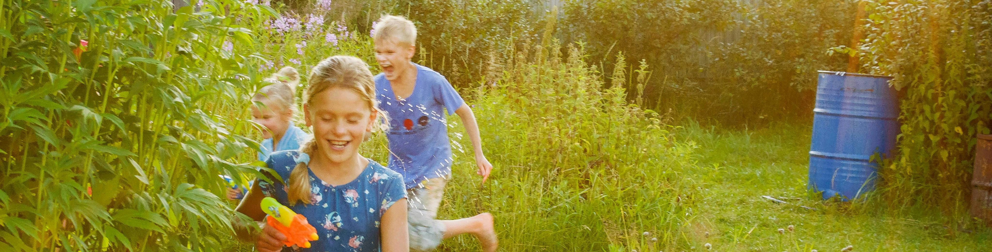 Drei Kinder beim Spielen mit Wasserpistolen im Garten