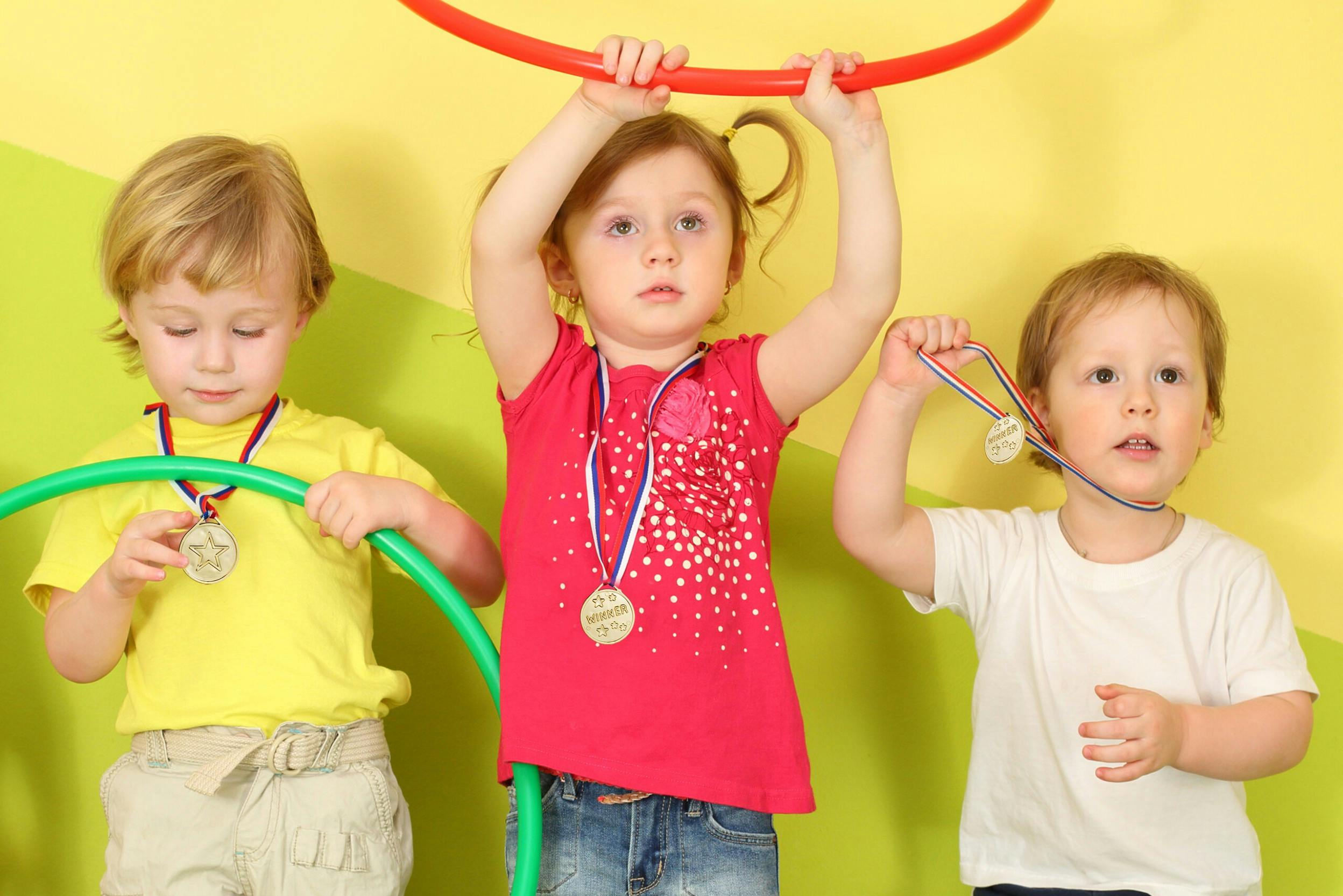 Drei Kinder mit Medaillen und bunten Hulahoop-Ringen