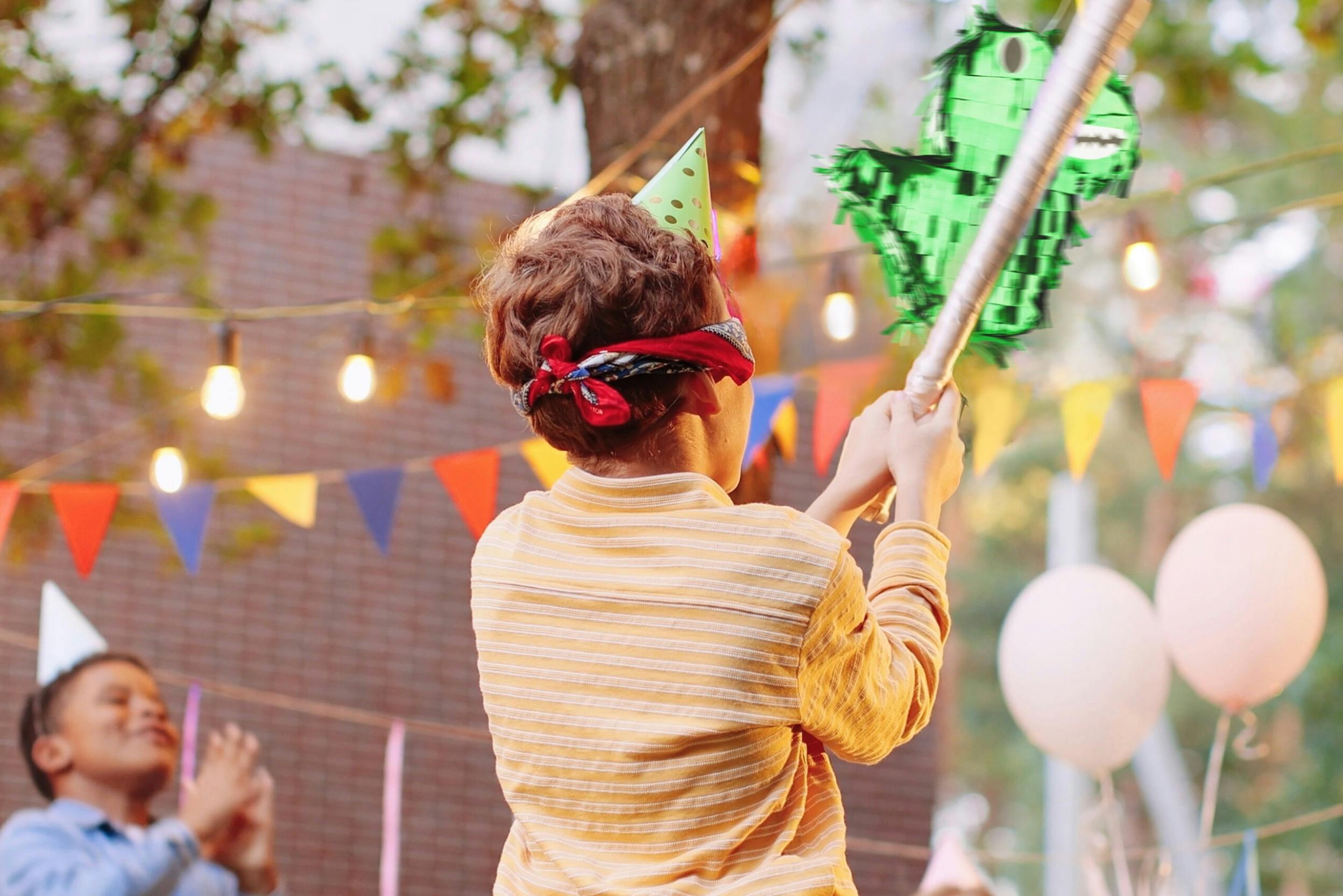 Junge mit verbundenen Augen schlägt auf eine Piñata in Form eines Dinosauriers