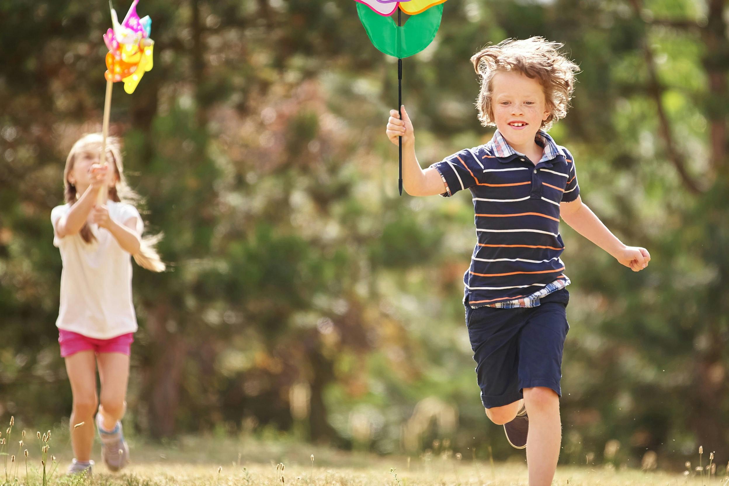 Junge und Mädchen laufen im Garten mit Windmühlen und Gartensteckern