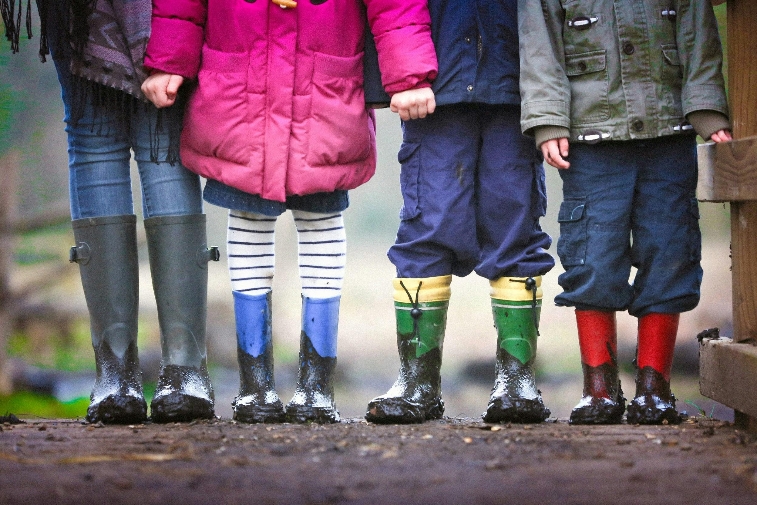 Vier Kinder in schmutzigen Gummistiefeln halten sich im Regen an den Händen