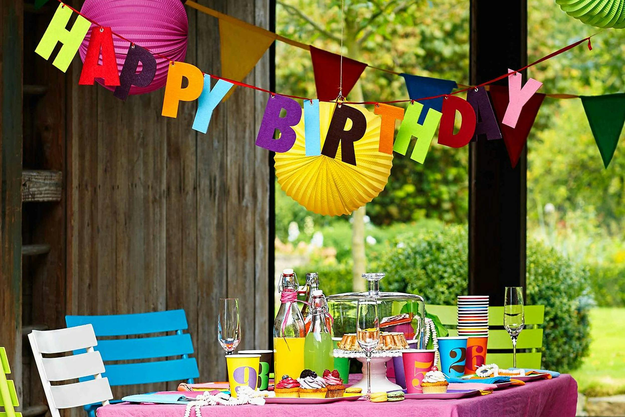 Bunt gedeckter Geburtstagstisch im Garten mit Happy-Birthday-Girlande