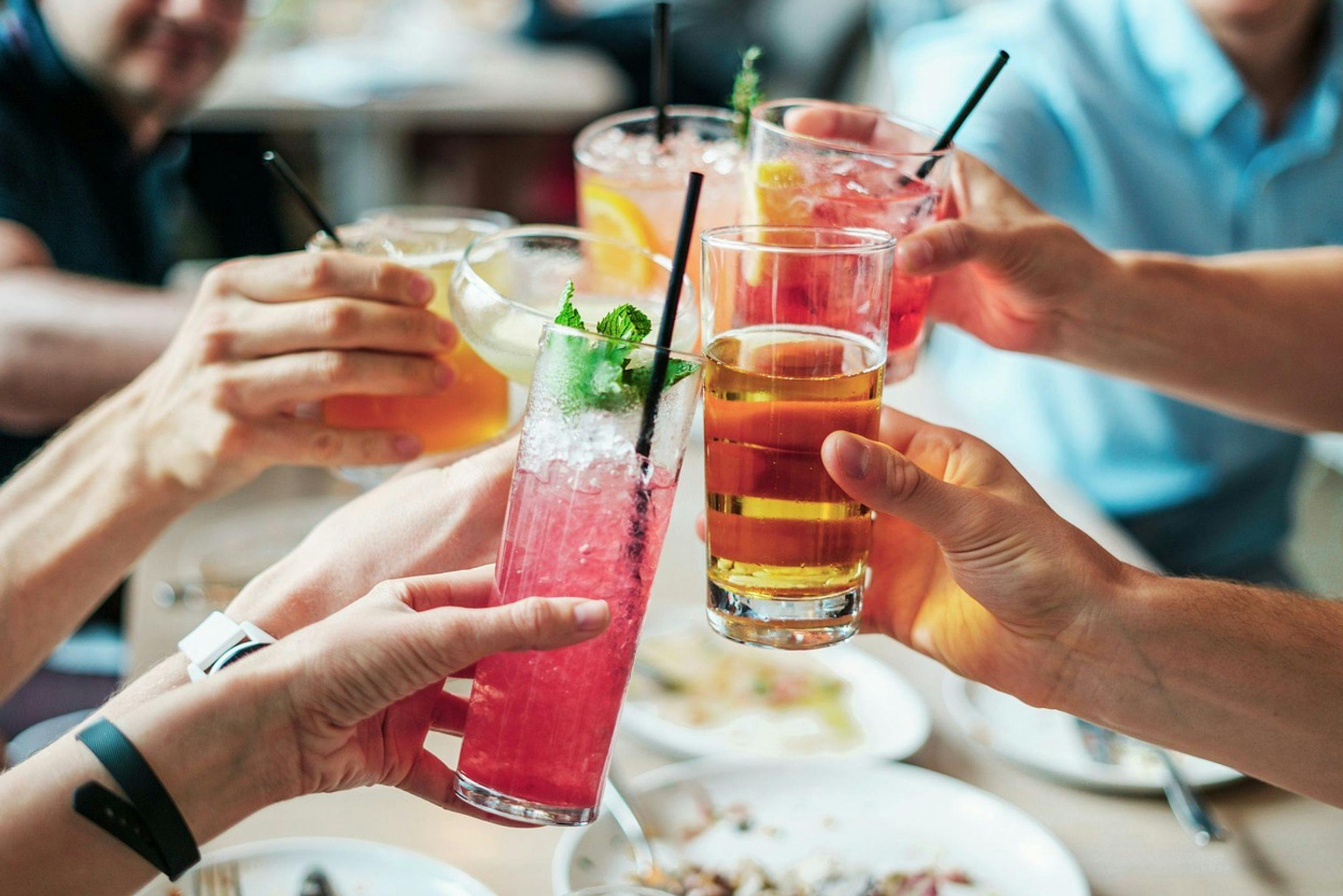 Plusieurs mains tenant des verres avec des boissons colorées et rafraîchissantes trinquant au-dessus d'une table avec des assiettes