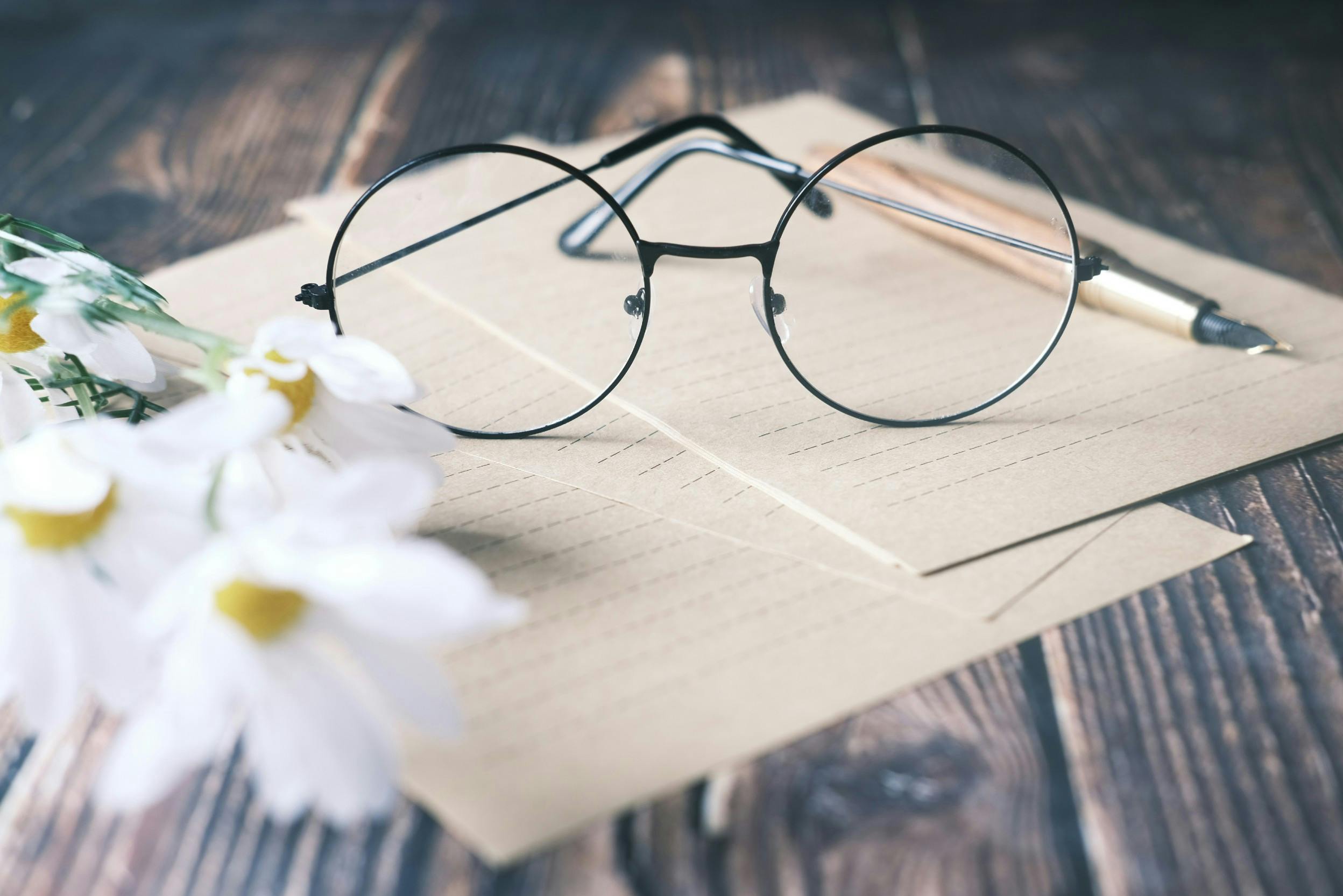 Am Black Friday klug einkaufen dank einer Einkaufsliste: Papier, Stift, Brille und Blumen liegen auf einem dunklen Massivholztisch.