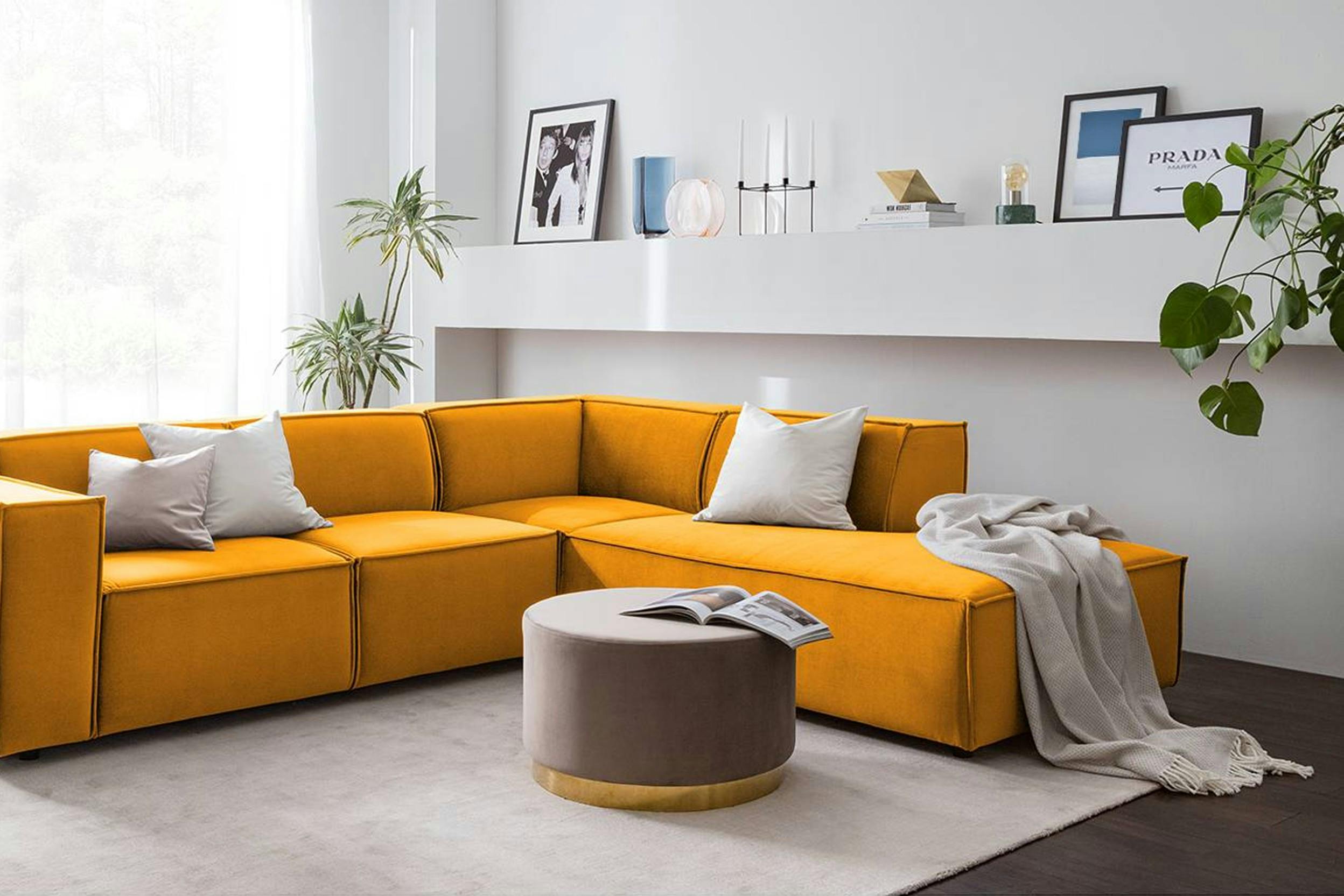 Gelbes Ecksofa mit grauem Pouf davor