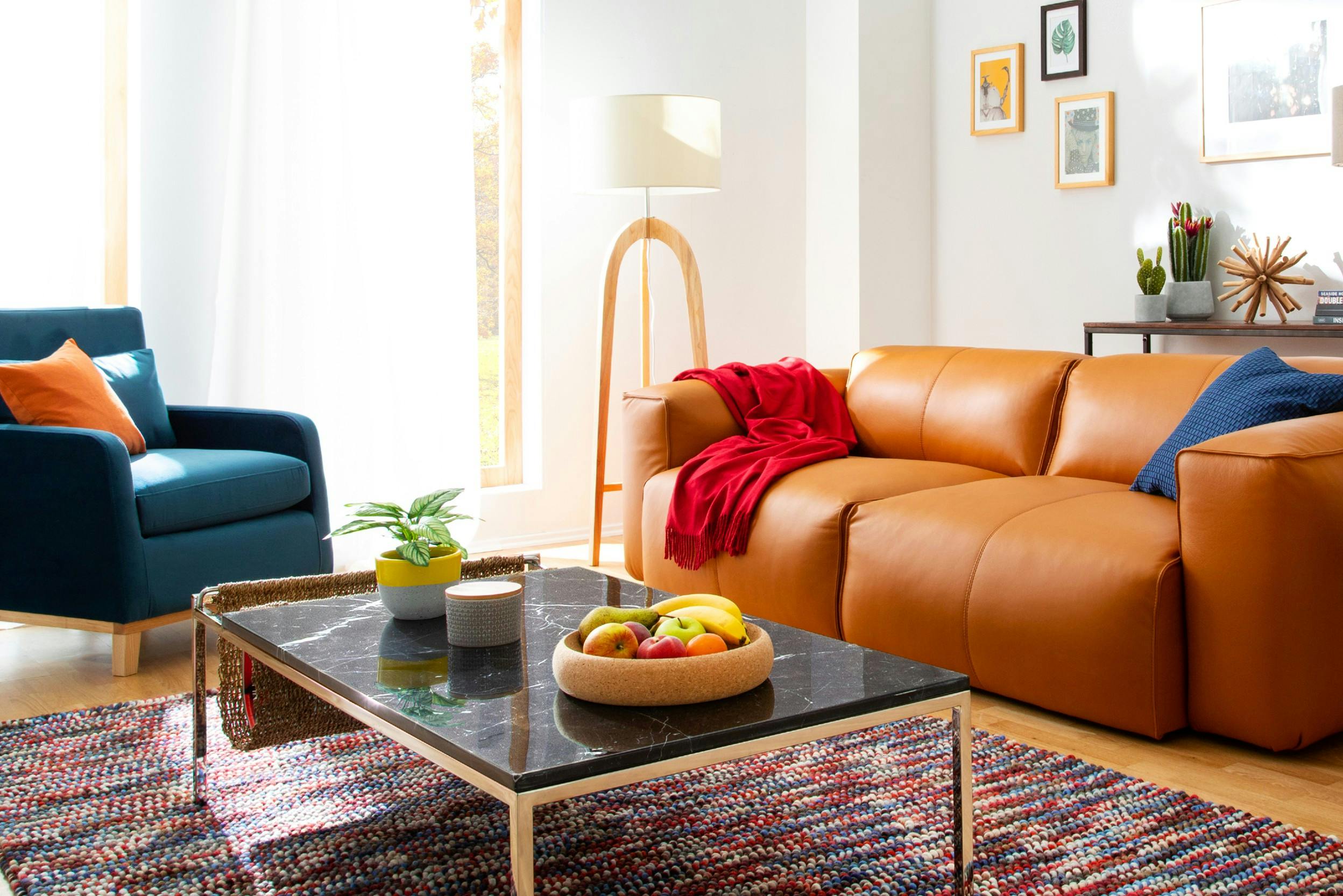 Wohnzimmer mit hellbrauer Couch, roter Decke und blauem Sessel