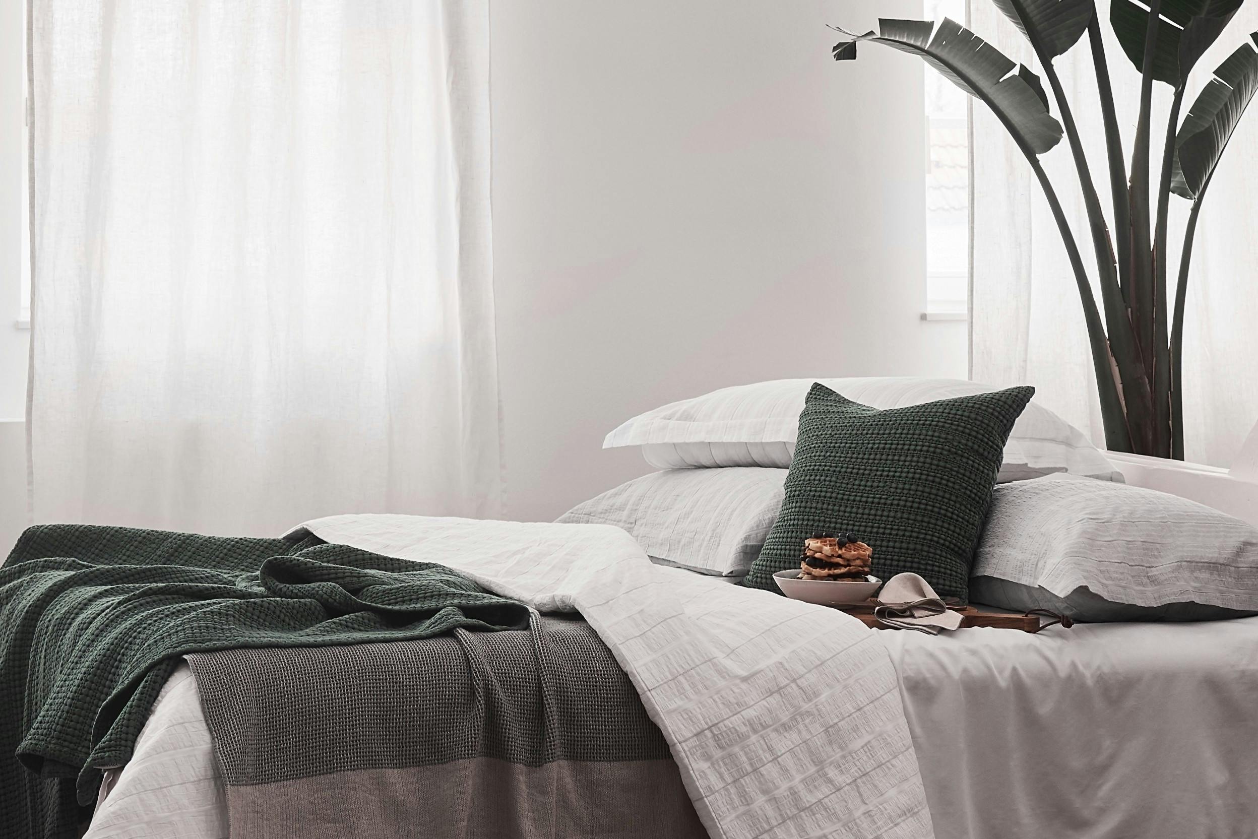 Seersucker-Bettwäsche in Weiß, dekoriert mit grünen Betttextilien neben einer großen Zimmerpflanze