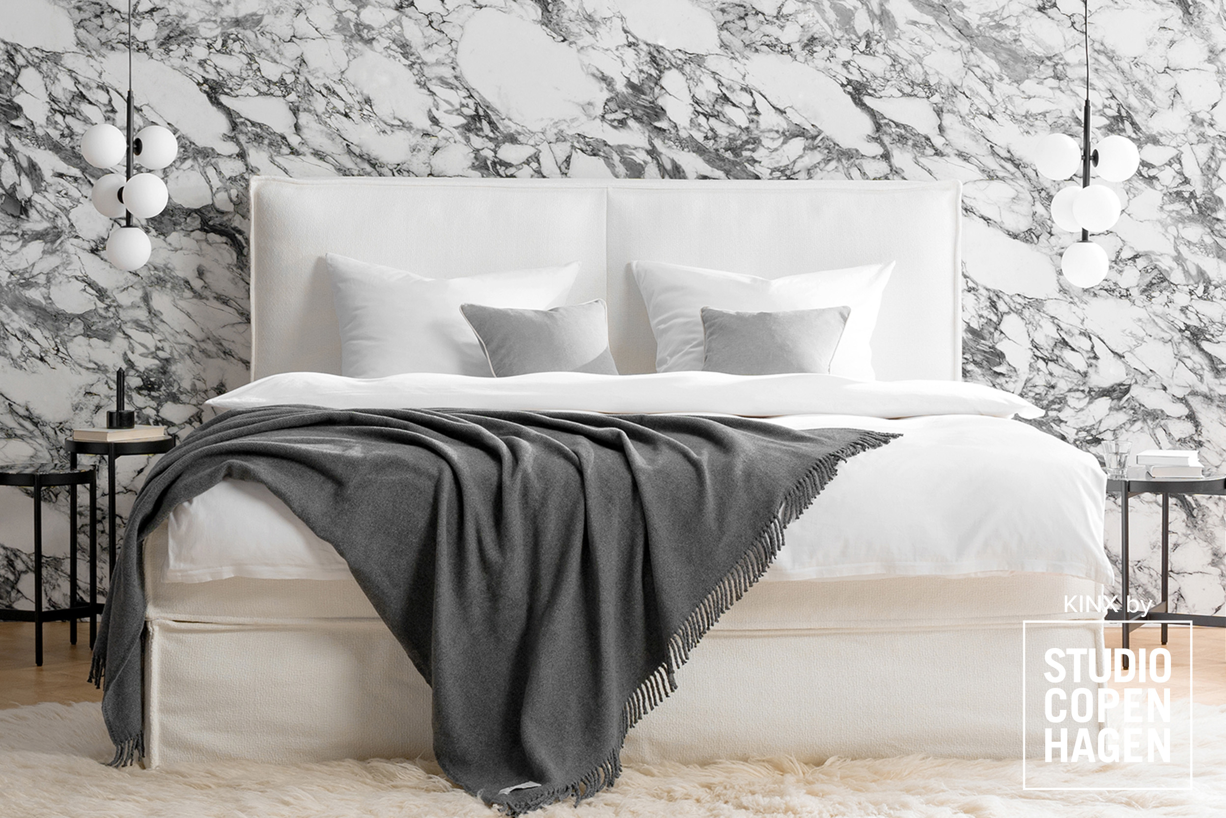 Cremefarbenes Boxspringbett KINX vor grau marmorierter Tapete