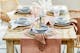 Gedeckter Brunchtisch, Esszimmermöbel aus natürlichem Echtholz und Rattangeflecht, Tafel eingedeckt mit Keramikgeschirr, rosa Glaskelchen, Goldbesteck auf einem Tischläufer aus Baumwollmusselin.