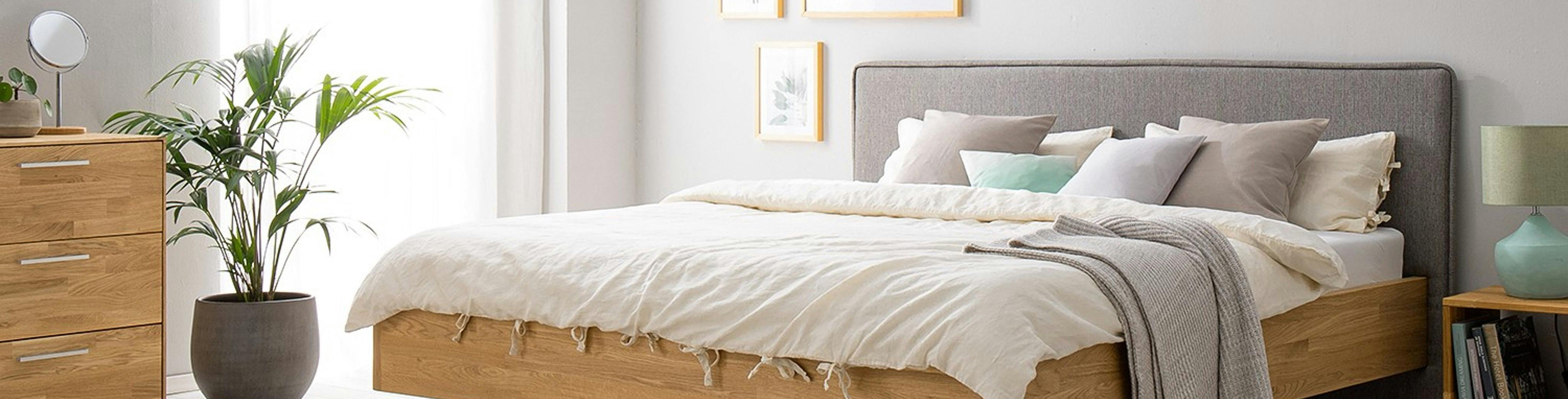 Holzbett mit gepolstertem Kopfteil in Grau, passende Schränke und große Zimmerpflanze