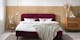 Schlafzimmer im Skandi-Stil mit dunkelrotem Polsterbett, Holzmöbeln und Glaslampe