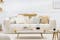 Salone in stile scandinavo con divano a due posti bianco, poltrona beige, sedia con braccioli e tavolino da salotto in legno chiaro su tappeto bianco