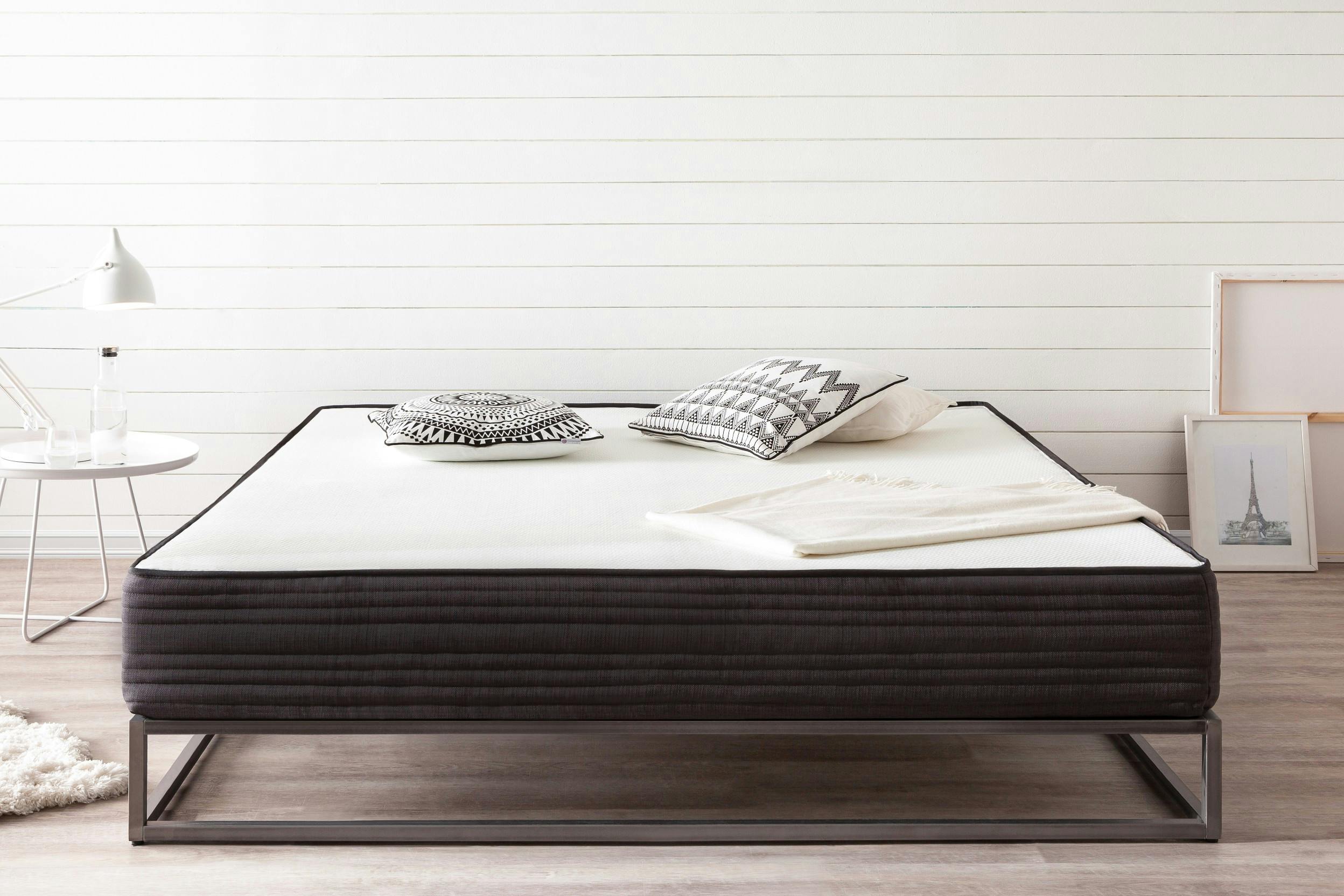 Matratze auf einem modernen Metallbettgestell, dekoriert mit schwarzen-weißen Kissen und Decke