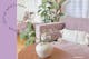 Lila bank met witte kussens in de boho-stijl, veel groene planten; daarnaast een foto van een glazen vaas met roze pioenrozen met op de achtergrond bloemetjesbehang.