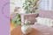 Lila bank met witte kussens in de boho-stijl, veel groene planten; daarnaast een foto van een glazen vaas met roze pioenrozen met op de achtergrond bloemetjesbehang.