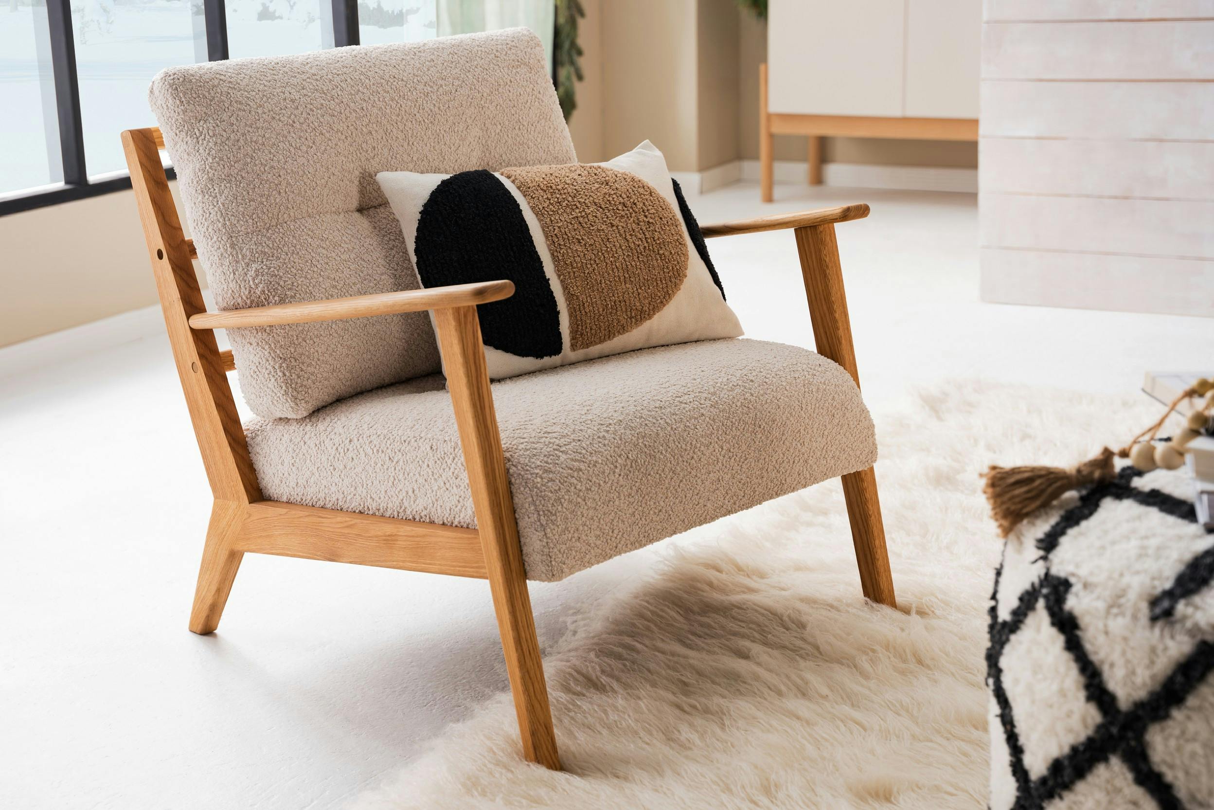 Sessel im skandinavischen Design aus einem Bouclé-Stoff mit einem Kissen darauf