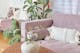 Lilafarbenes Sofa mit weißen Kissen im Boho-Style, dazu viele Grünpflanzen; daneben eine Glasvase mit rosa Pfingstrosen, dahinter eine Blumentapete.