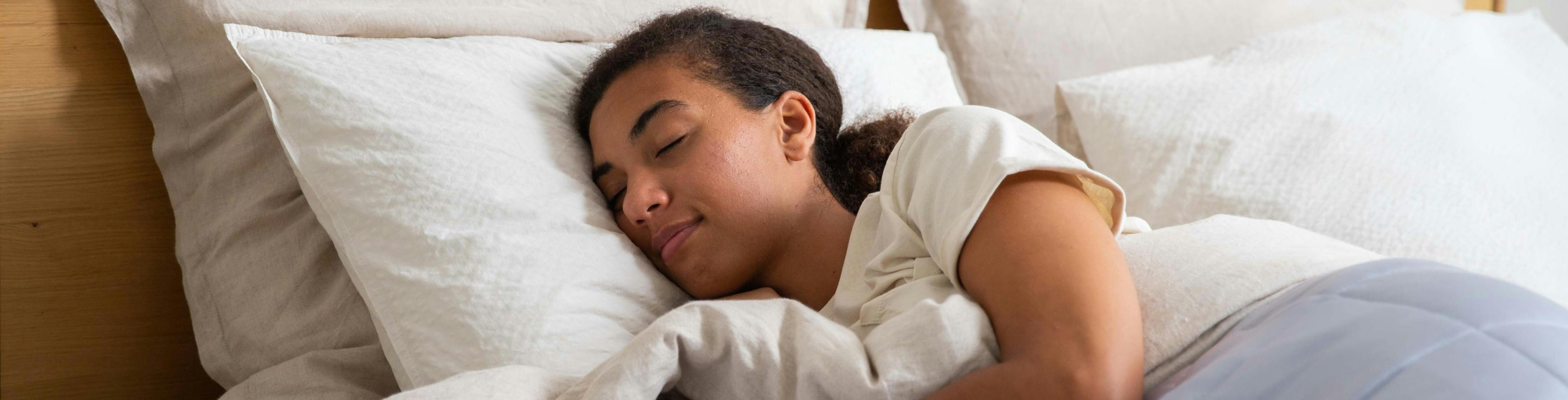 Junges Mädchen beim Schlafen in einem Holzbett mit vielen luftigen Kissen