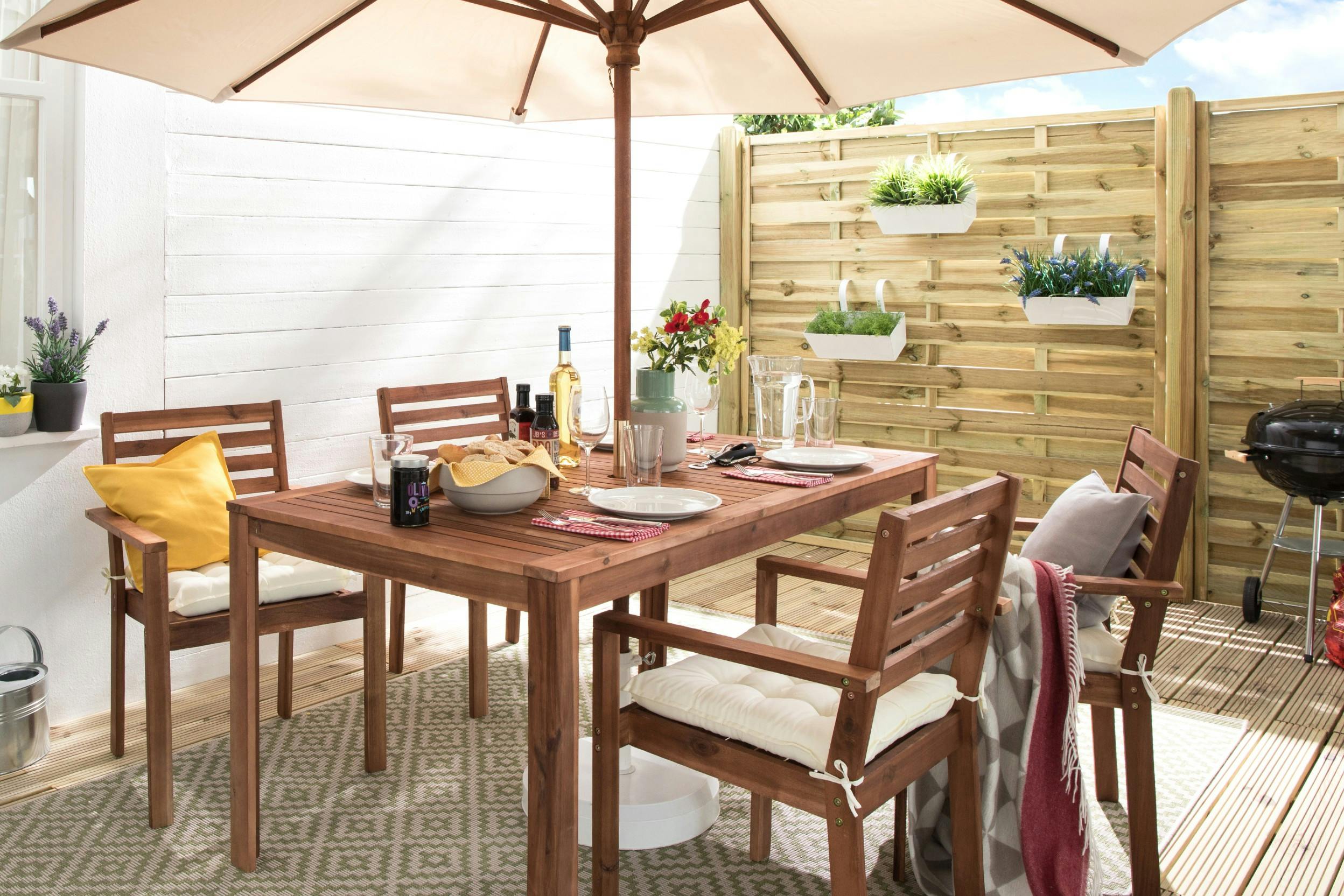 Terrasse mit Sitzgruppe aus Holz, aufgespanntem Sonnenschirm und Kugelgrill