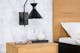 Zwarte wandlamp met lantaarndesign boven een eikenhouten nachtkastje en zwart metalen meubelpoten.